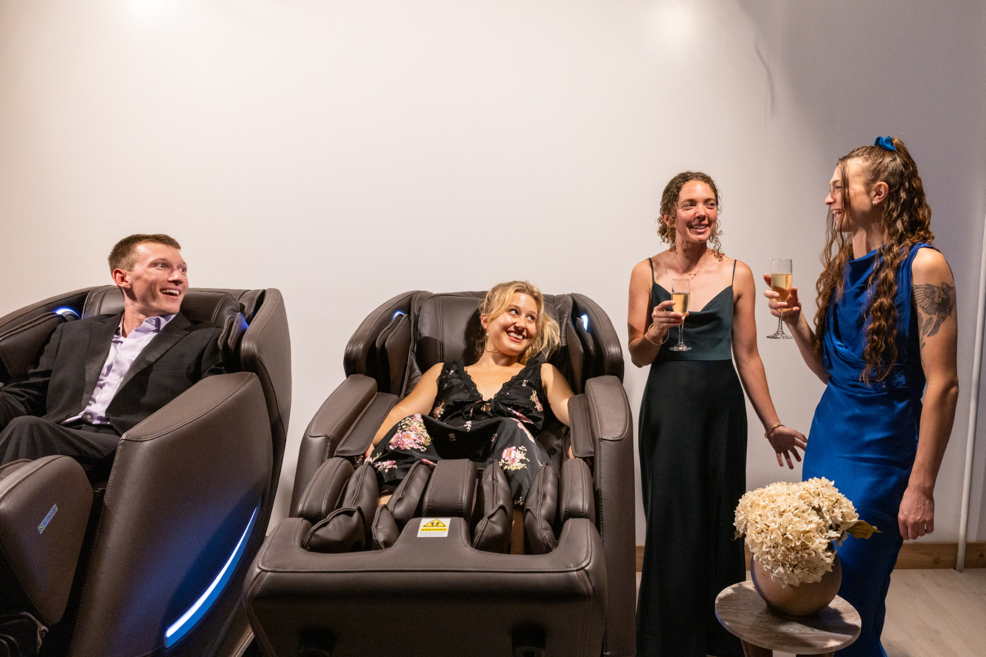 Two guests in massage chairs talking with two women in evening gowns holding champagne flutes